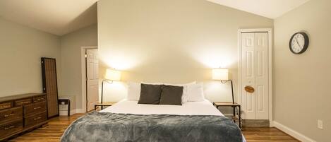 A bedroom with a bed, two bedside lamps, a clock on the wall, and a door.
