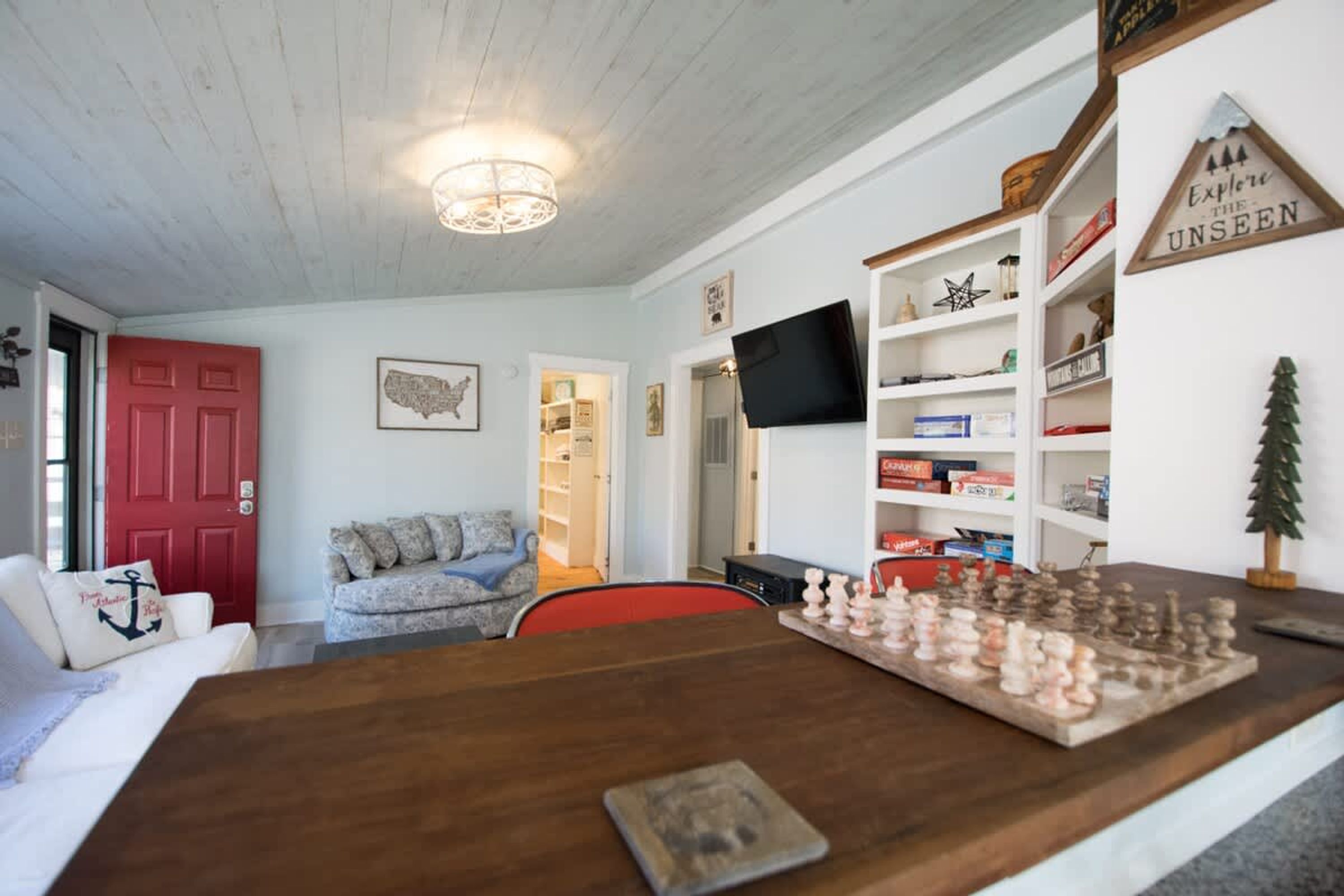 Uma sala de estar aconchegante com uma mesa de centro de madeira, uma porta vermelha, uma televisão e uma estante de livros.