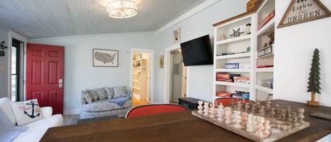 Un salon chaleureux avec une table basse en bois, une porte rouge, un téléviseur et une bibliothèque.