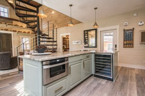 A spacious kitchen with a central island, stainless steel appliances, and a wooden staircase. - Rustic Awesome 4BR Lodge w Game Room Fire Pit (Hendersonville)