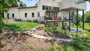 A modern two-story house with a flat roof, large windows, and a balcony with outdoor furniture. - Luxe 5BR w Home Theater Pool Table Firepit (Alexander)