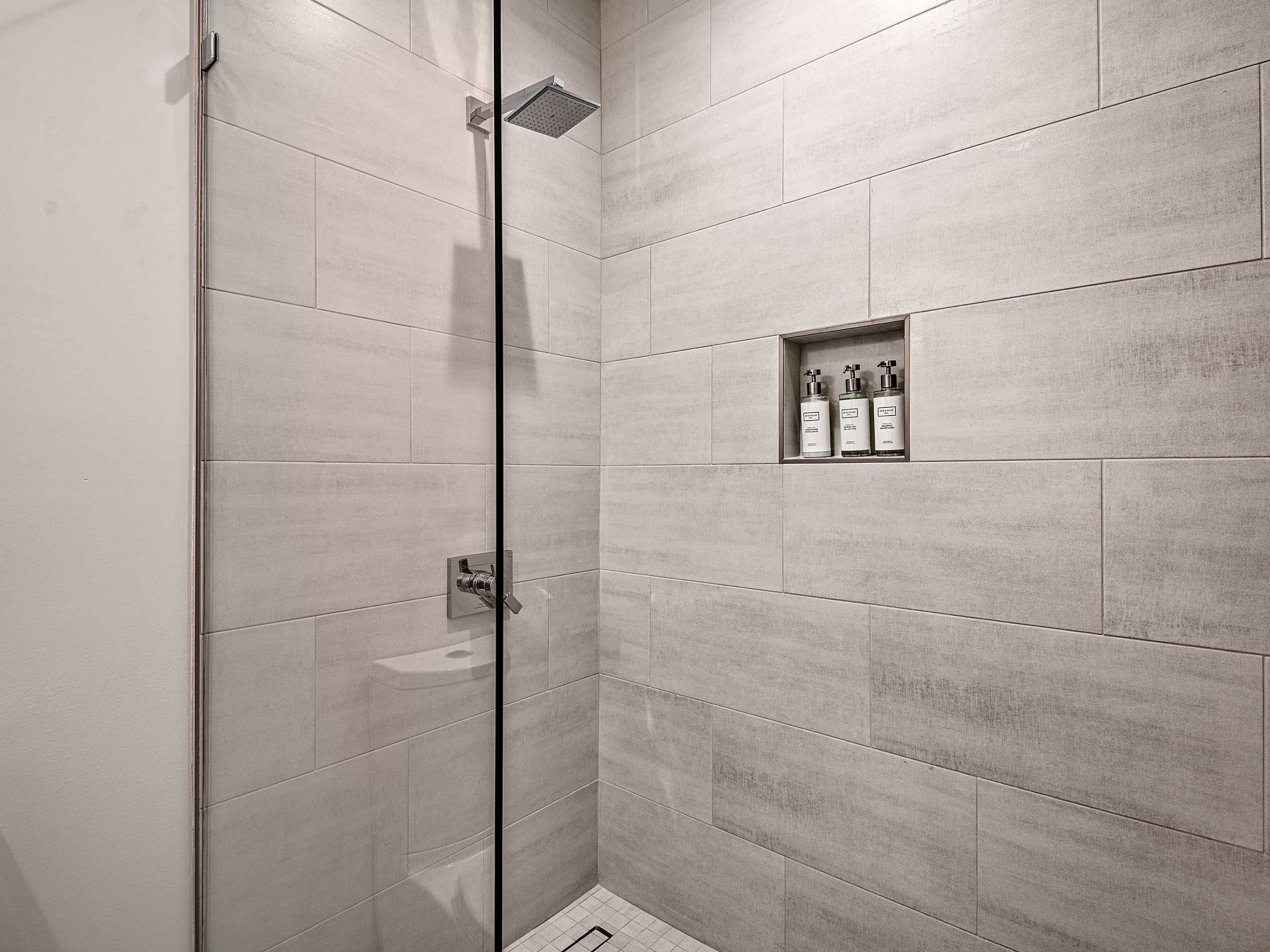 Ein modernes Duschbad mit Glastür, integriertem Ablagefach für Toilettenartikel und Fliesenwand.