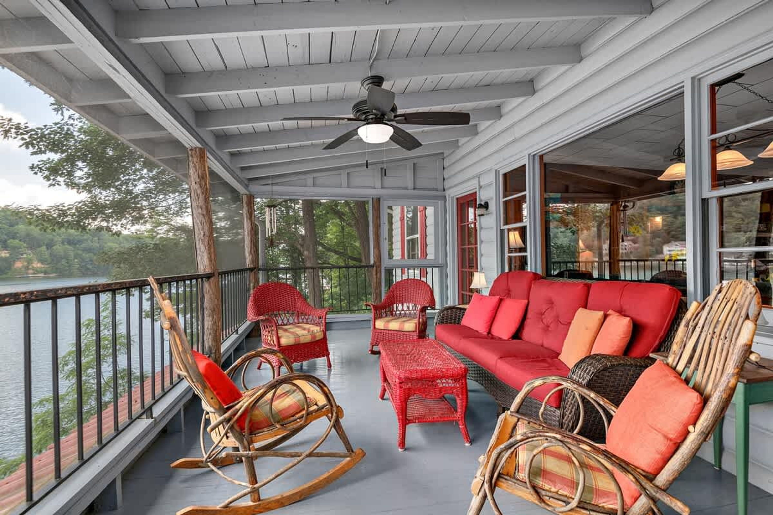 A covered porch with wicker furniture, a red sofa, and a ceiling fan.