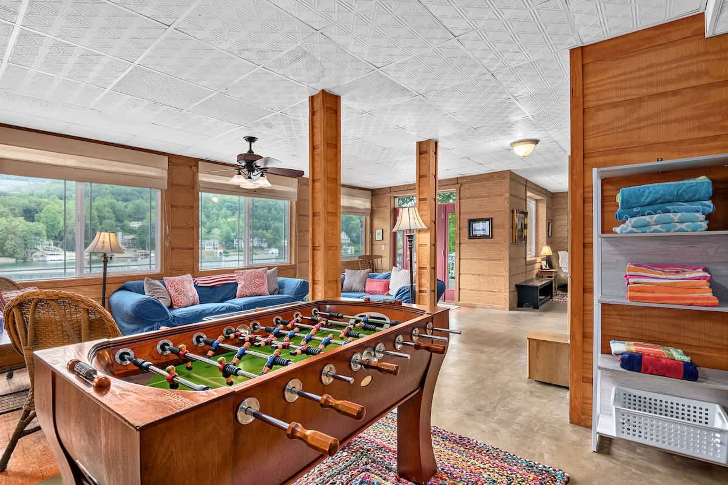 A spacious room with a wooden foosball table, a sofa, and a shelf with folded blankets.