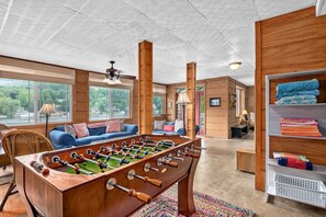 A spacious room with a wooden foosball table, a sofa, and a shelf with folded blankets. - Lakeside 4BR Mountain Views Firepit Game Room (Lake Lure)