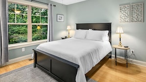 A bedroom with a bed, a ceiling fan, two bedside tables with lamps, a window with curtains, and a view of greenery outside. - Cozy 2BR Townhouse w Deck Walk to W Asheville (Asheville)