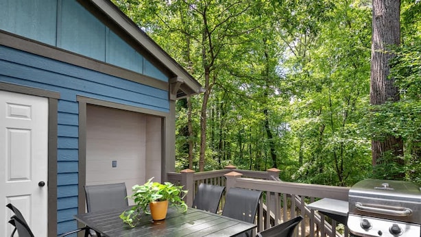 An outdoor deck with a table and chairs, a grill, and a blue building in the background. - Cozy 2BR Townhouse w Deck Walk to W Asheville (Asheville)