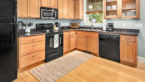 A modern kitchen with wooden cabinets, a black refrigerator, a microwave, a stove, and a dishwasher. - Cozy 2BR Townhouse w Deck Walk to W Asheville (Asheville)