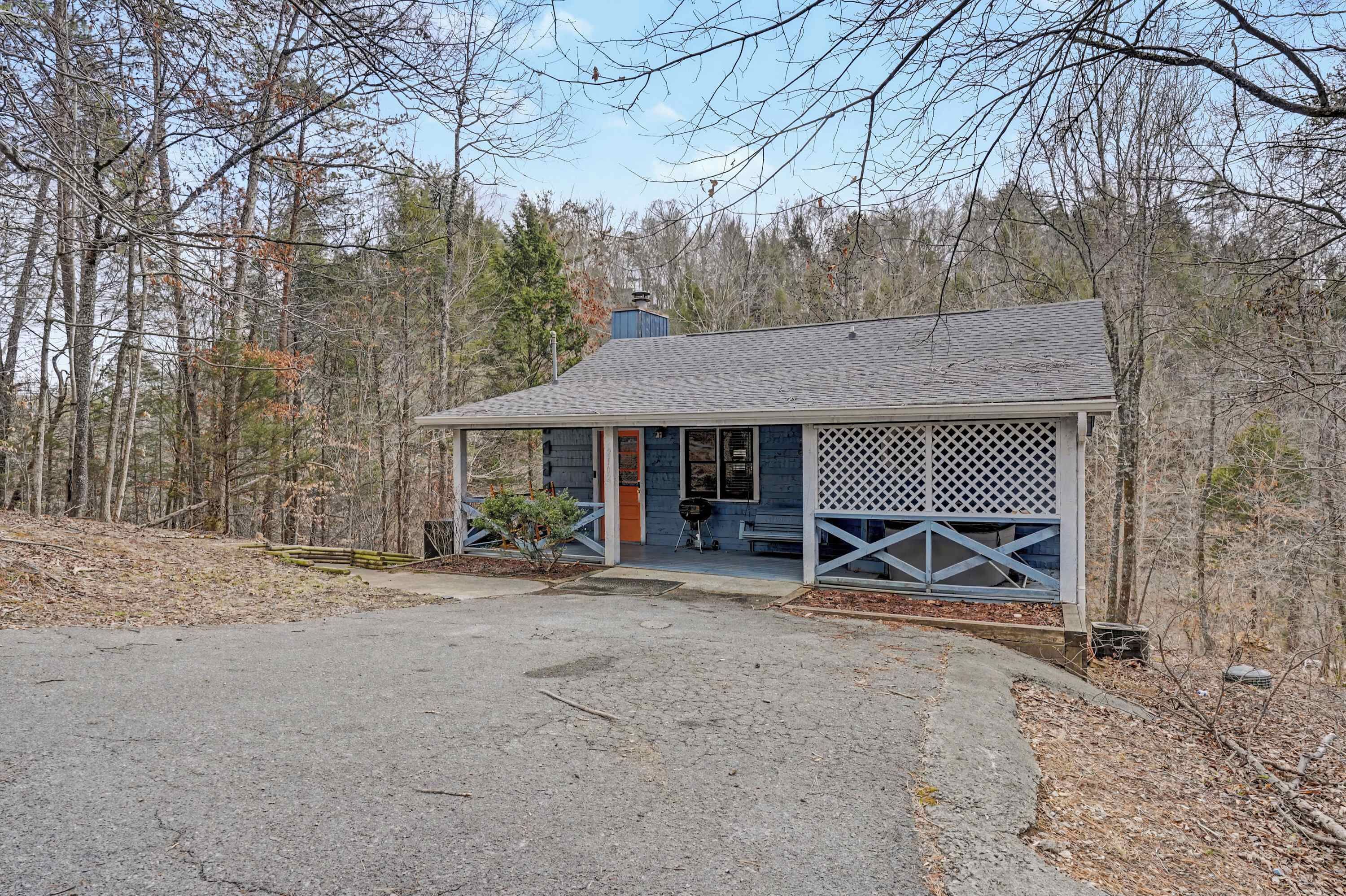 A small, single-story building with a porch and a lattice screen, surrounded by trees.