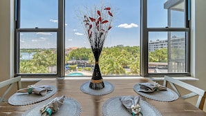 Ein Esstisch mit Untersetzern und einer Vase mit roten Blumen, vor einem großen Fenster mit Blick auf Stadt und Grünflächen.