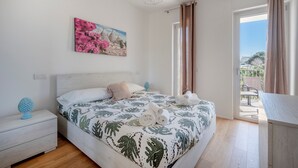 Un dormitorio con cama, mesita de noche, un cuadro y vista a través de una puerta abierta.