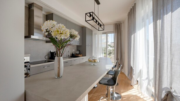 Una cocina moderna con una isla central, taburetes de bar y un jarrón con flores.