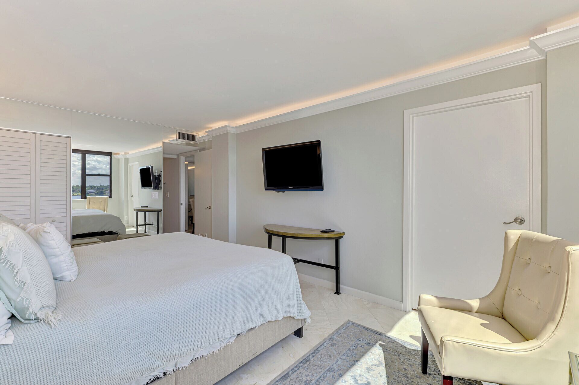 A hotel room with a large bed, a television mounted on the wall, a chair, and a small table.