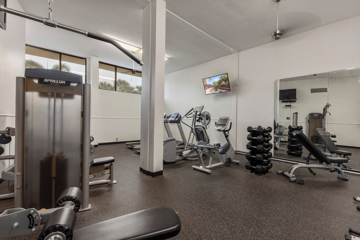 Ein Fitnessraum mit unterschiedlichen Trainingsgeräten, einem Fernseher und einem großen Spiegel.