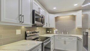 Una cocina moderna con armarios blancos, microondas integrado, electrodomésticos de acero inoxidable y salpicadero de azulejos.