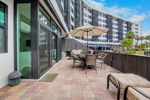 A modern hotel patio with a dining area, outdoor seating, and a large umbrella. - Harbor Towers 131 - Tropical Sands Accommodations (Siesta Key)