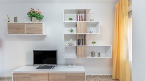 Een moderne woonkamer met een flatscreen televisie, een witte salontafel en ingebouwde planken met decoratieve objecten.