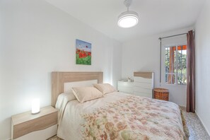 Ein Schlafzimmer mit Bett, Nachttisch, Kommode und einem Fenster mit Vorhängen.