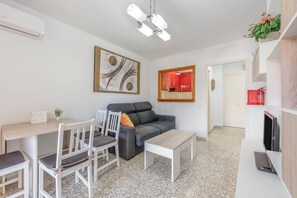 Ein modernes Wohnzimmer mit einem grauen Sofa, weißen Stühlen, einem Couchtisch und einem Esstisch.