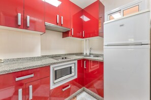 Eine Küche mit roten Schränken, einer eingebauten Mikrowelle und einem weißen Kühlschrank.