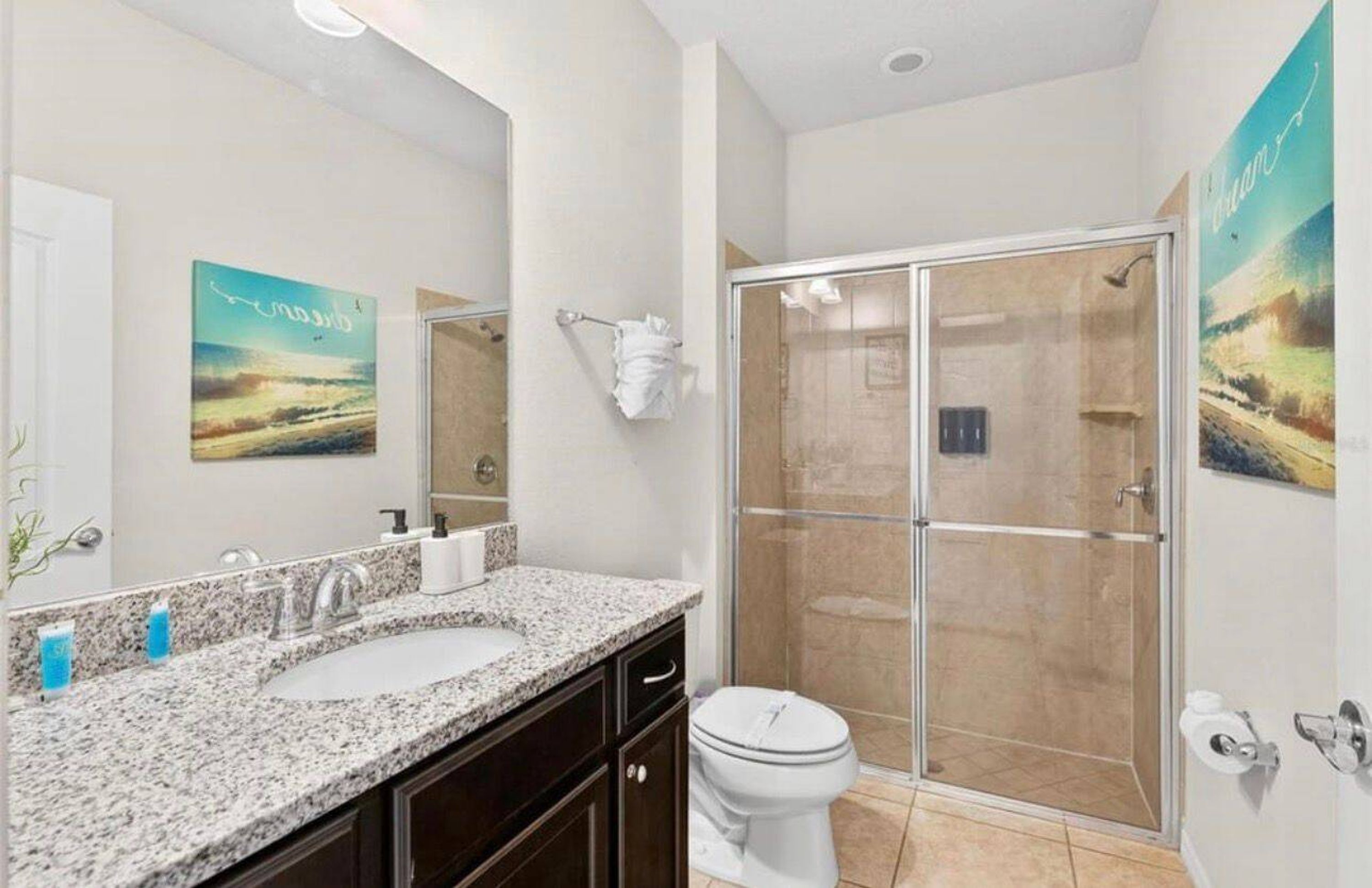 A bathroom with a granite countertop sink, a toilet, and a glass-enclosed shower.