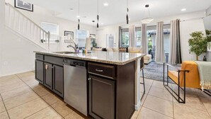 A modern kitchen with a central island, dark cabinetry, and pendant lighting. - Go 17 Windsor at Westside (Kissimmee)