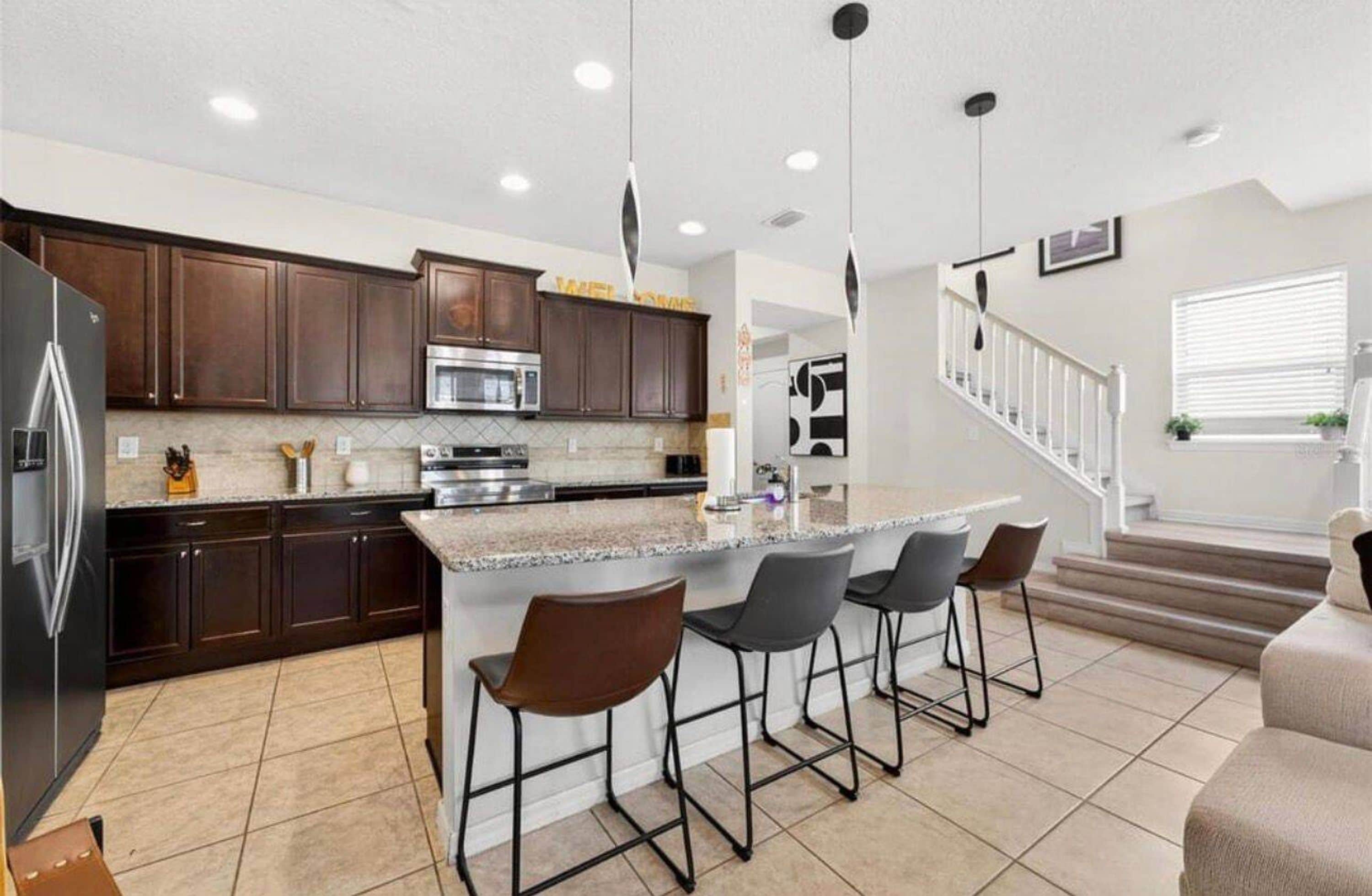 A modern kitchen with dark wood cabinets, stainless steel appliances, and a central island with bar stools.
