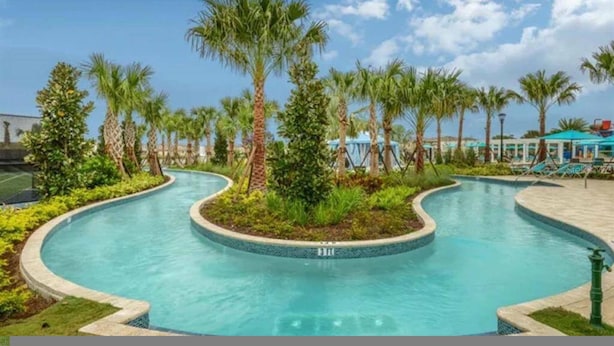 A pool area with palm trees, a curved pool, and lounge chairs. - Go 17 Windsor at Westside (Kissimmee)