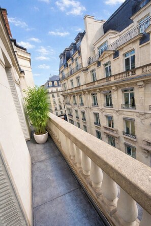 Ein schmaler Balkon mit einem Blumentopf, der auf eine Reihe von mehrstöckigen Gebäuden mit Balkonen und Fenstern blickt.
