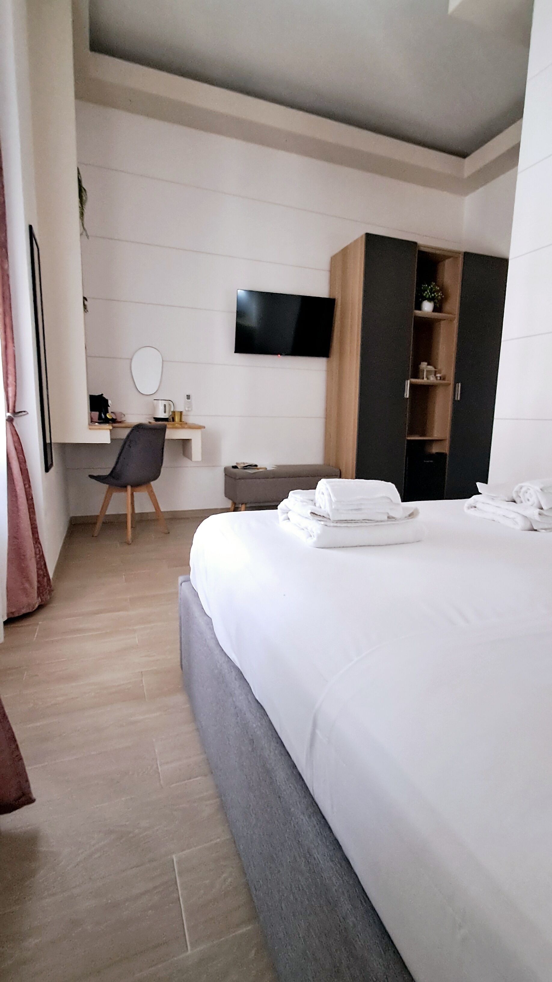 A modern hotel room with a large bed, a desk with a flat-screen TV, a chair, and a wardrobe.