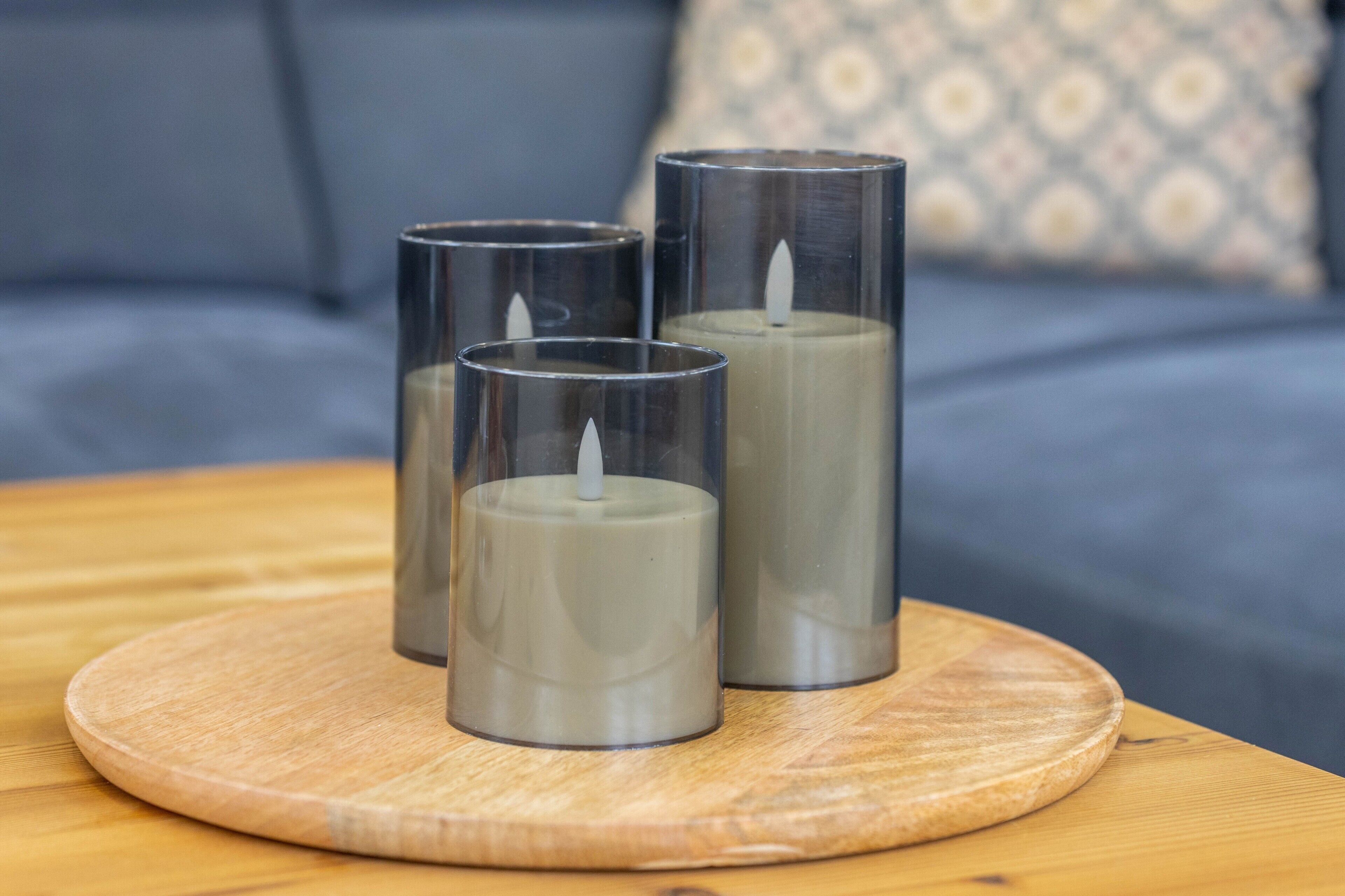 Drie cilindervormige kaarsen op een houten onderzetter op een tafel.