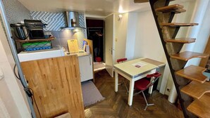 A compact kitchen with a microwave, coffee maker, and a small countertop. There is a dining area with a table and chairs, and a wooden staircase to the right. - STUDIO NOTRE DAME - Latin Quarter (Paris)