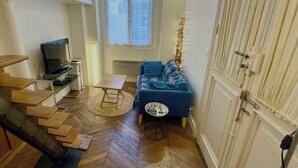 A compact living space with a sofa, a small table, a TV, and a staircase. - STUDIO NOTRE DAME - Latin Quarter (Paris)