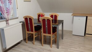 A dining area with a table and four chairs, a small refrigerator, and a window with a view of trees. - Cozy vacation apartment in the countryside (Wertheim)