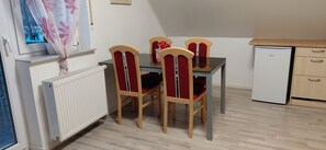 A dining area with a table and four chairs, a small refrigerator, and a window with a view of trees. - Cozy vacation apartment in the countryside (Wertheim)