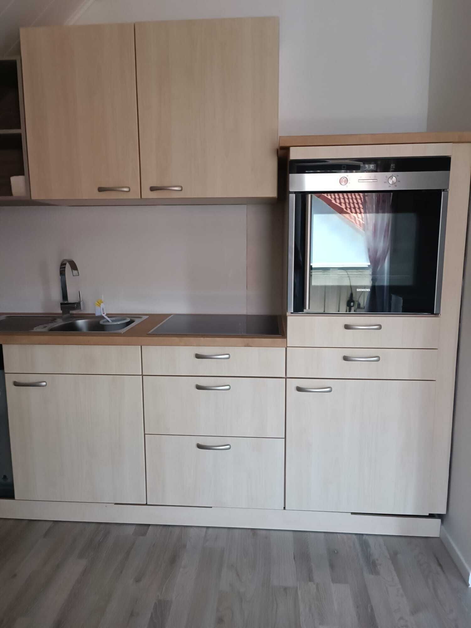 A modern kitchen with light wood cabinets, stainless steel appliances, and a built-in oven.