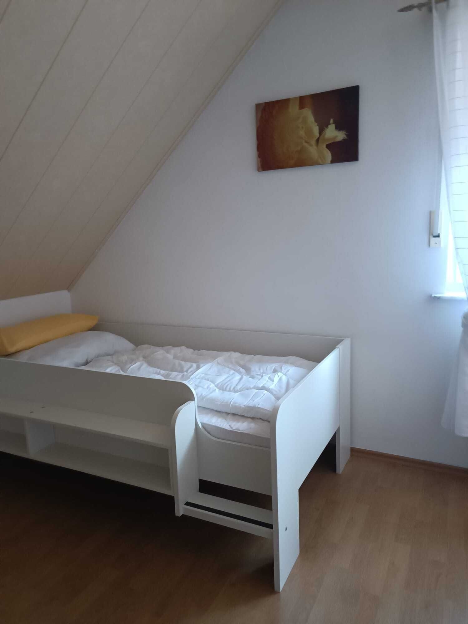 A small, white, single-bed room with a sloped ceiling and wooden flooring.