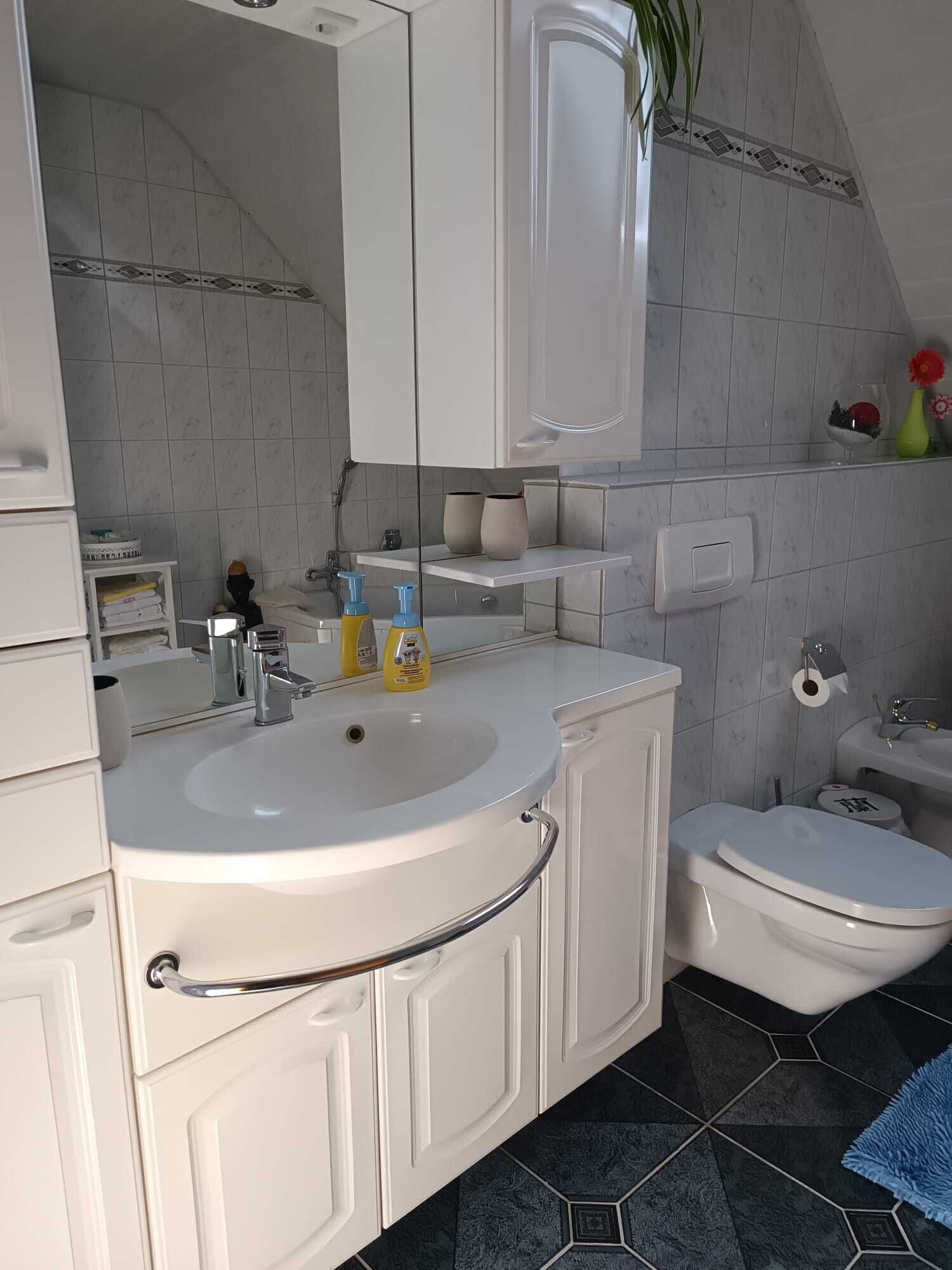 Een badkamer met een wit wastafel, spiegel en toilet. Er liggen toiletartikelen op de wastafel en er is een handdoekrek.