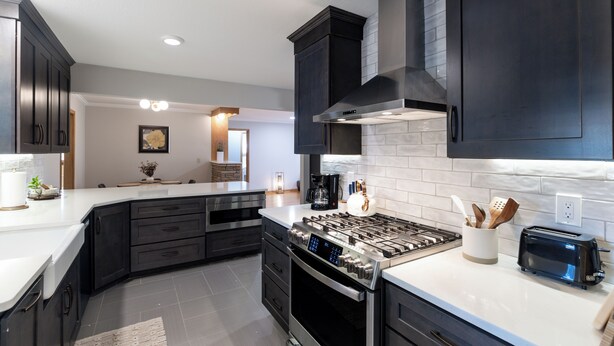 Una cocina moderna con armarios oscuros, una estufa de acero inoxidable y un horno empotrado.
