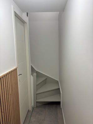 Ein schmaler Korridor mit einer Holzverkleidung links und einer weißen Wand rechts.