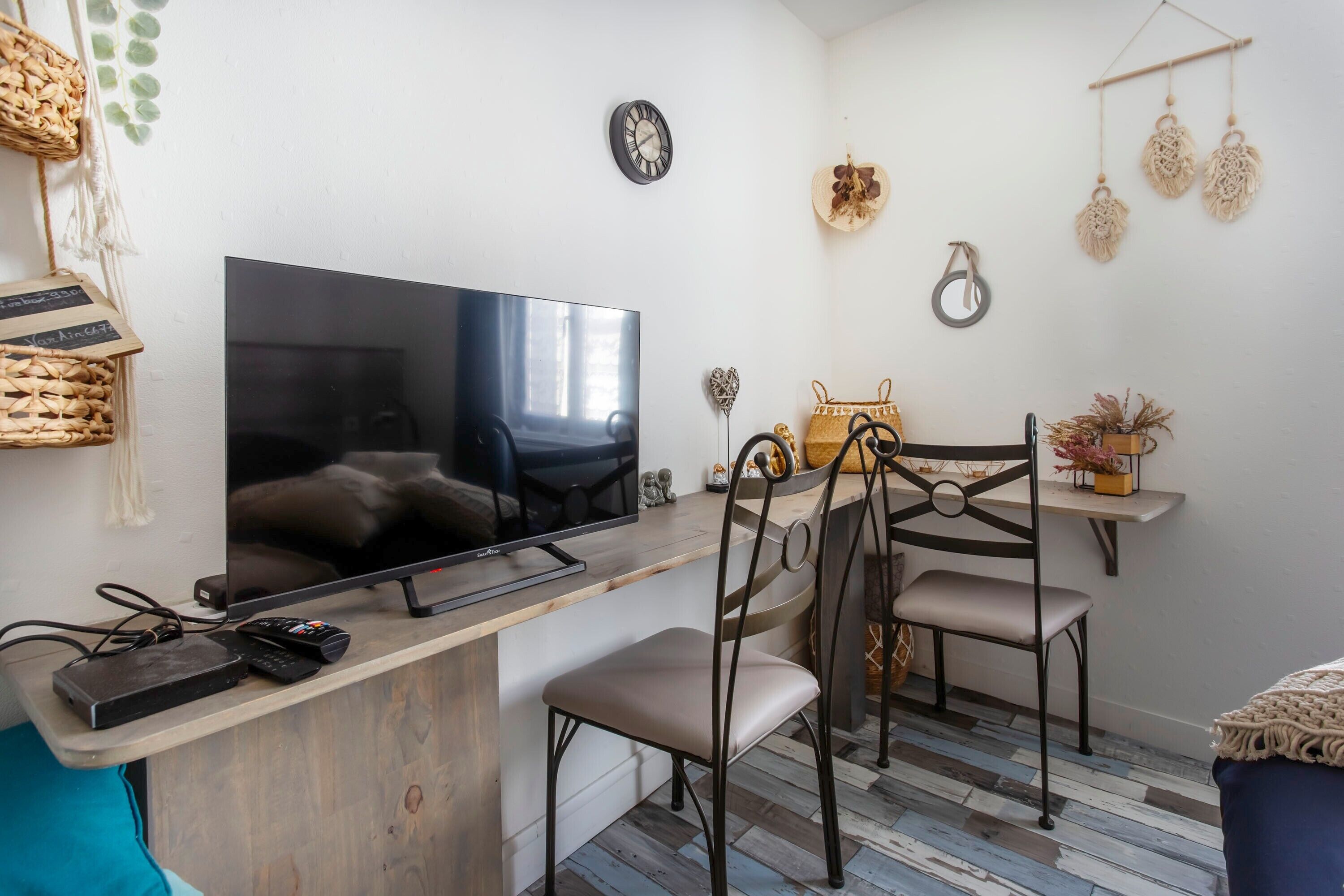 Un salon moderne avec un téléviseur à écran plat, une table basse en bois, deux fauteuils, une petite table d’appoint et des éléments décoratifs fixés au mur.