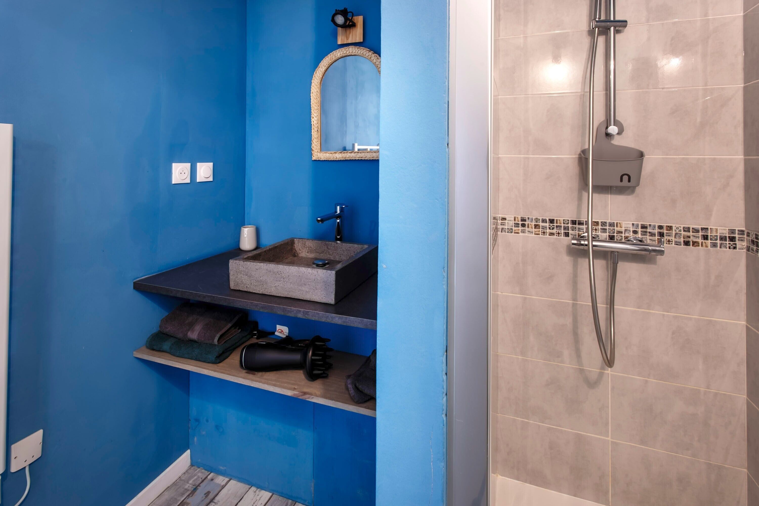 A bathroom with a blue wall, a sink with a stone basin, a mirror, and a shower area.