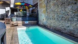 Ein Pool mit Holzterrasse, Steinmauer und Sitzgelegenheiten im Freien.