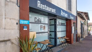 Ein Restaurant mit Außenbestuhlung, ein Schild mit dem Hinweis, dass es sich um ein Café handelt, und ein Schild für 'CHAMBRES D'HÔTES'.