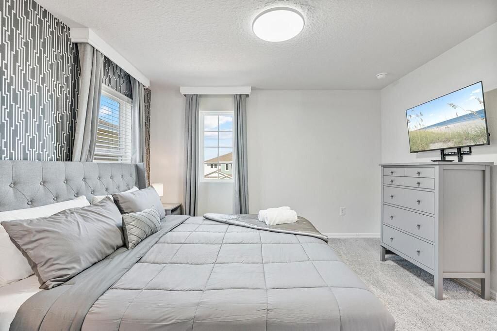 A bedroom with a large bed, a dresser, a television, and a window with curtains.
