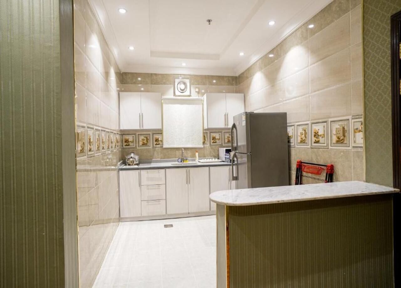 A modern kitchen with white cabinets, a marble countertop, and a refrigerator.