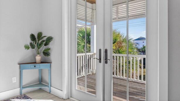 A corner room with a white door, a small blue table with a plant, and a view of a wooden deck and palm trees outside. - Huge Waterfront Home - Sleeps 20, private pool (gulf shores)