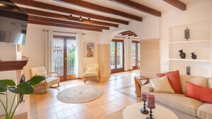 A spacious living room with a TV, comfortable seating, a fireplace, and a balcony with doors leading outside. - House "Valldemossa Paradise". (Valldemossa)