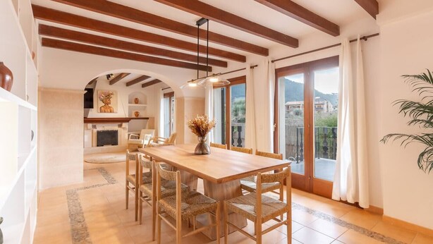 A dining area with a wooden table and chairs, a vase with dried flowers, and a view through a glass door to the outside. - House "Valldemossa Paradise". (Valldemossa)