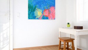 Ein Zimmer mit weißer Wand, Holzboden, einem weißen Tisch mit einer grünen Pflanze und einem farbenfrohen Gemälde.